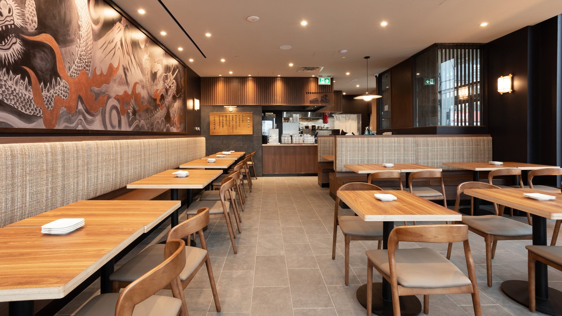 Modern restaurant interior with wooden tables, tan chairs, warm lighting, and minimalist Asian-inspired decor